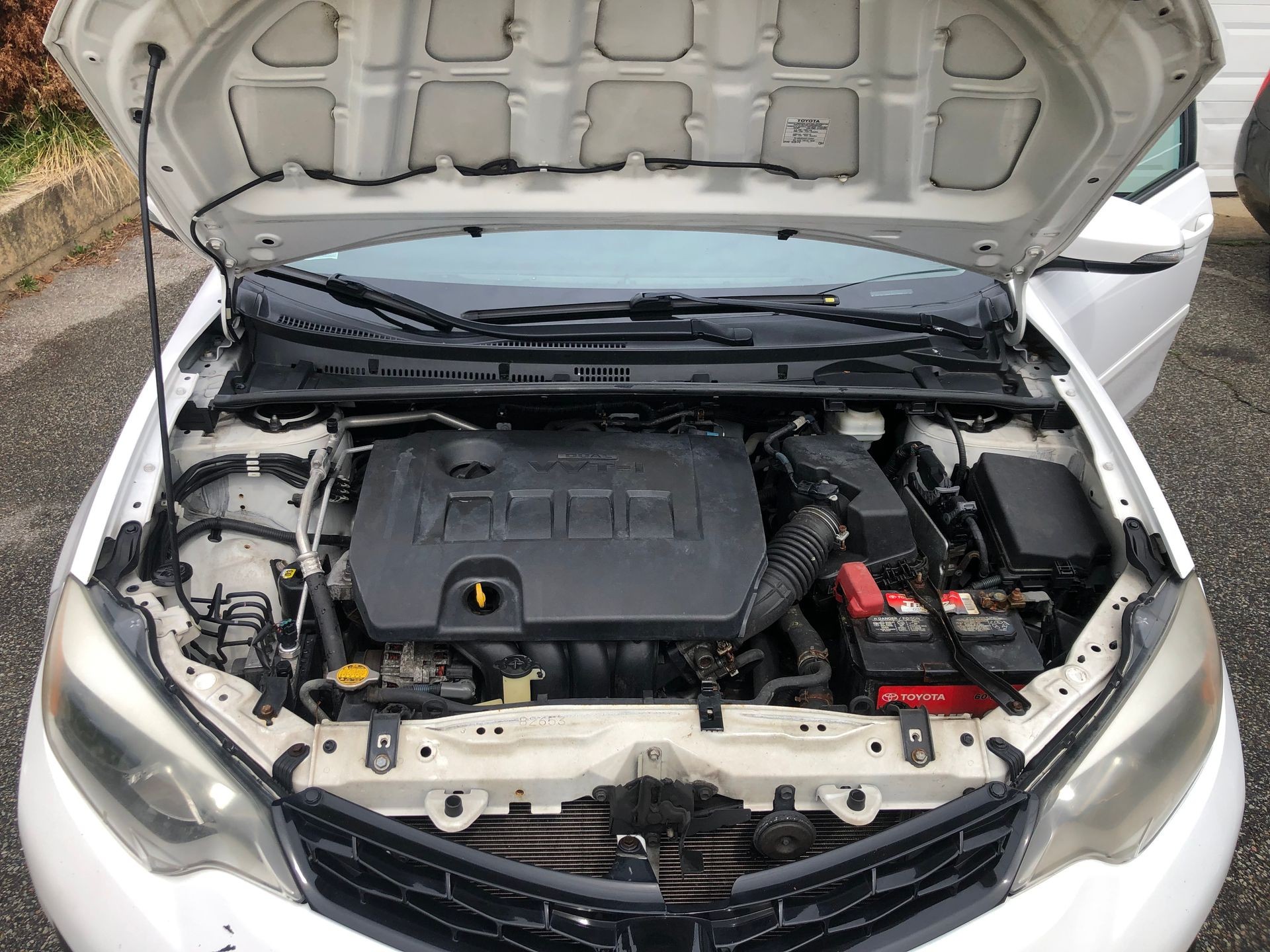 Open hood of a white car showing the engine and various components inside.